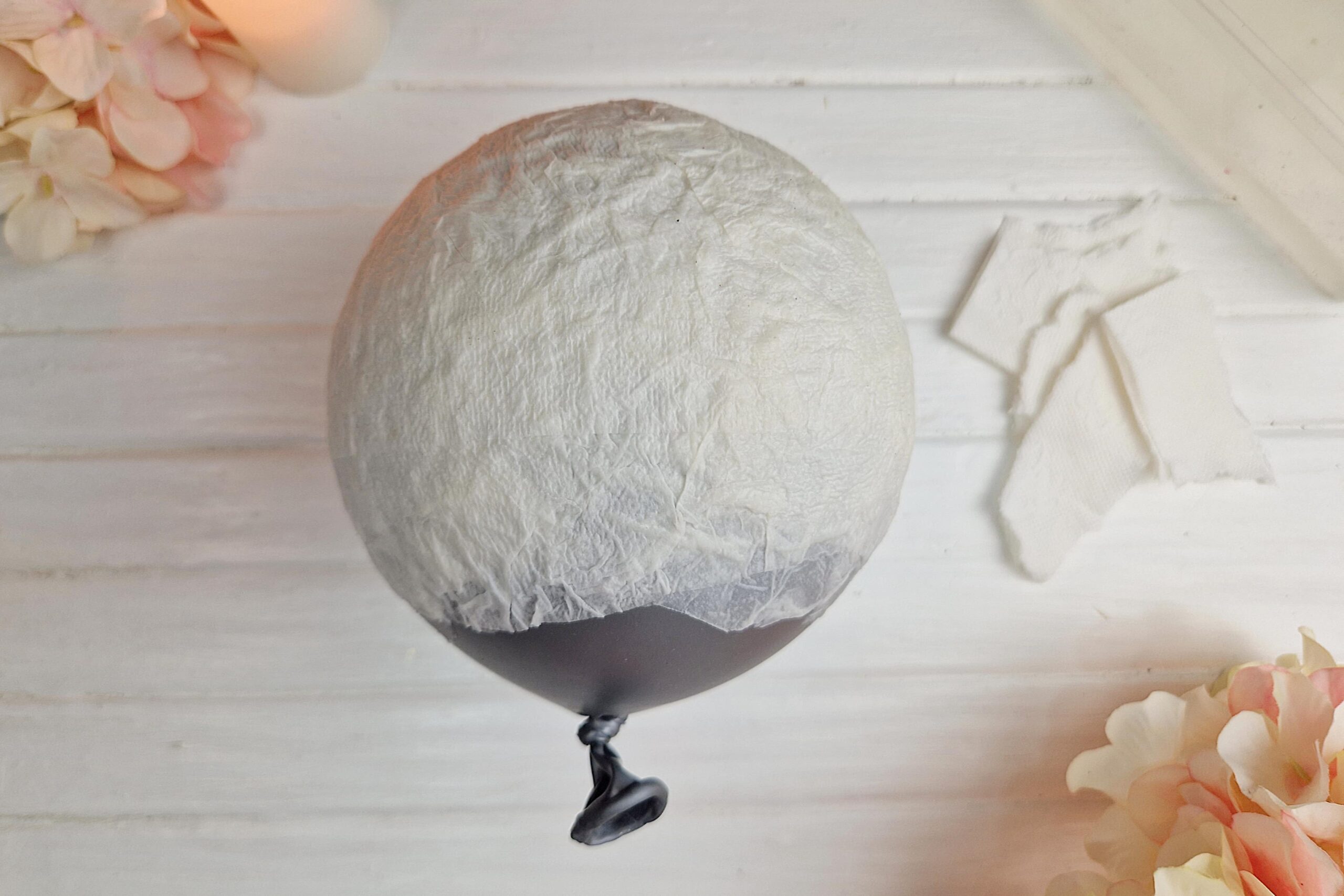 Die Bastelanleitung zeigt wie ein Luftballon mit Klopapier belegt wird, um daraus eine DIY Pilzlampe mit Blumen daraus zu basteln.